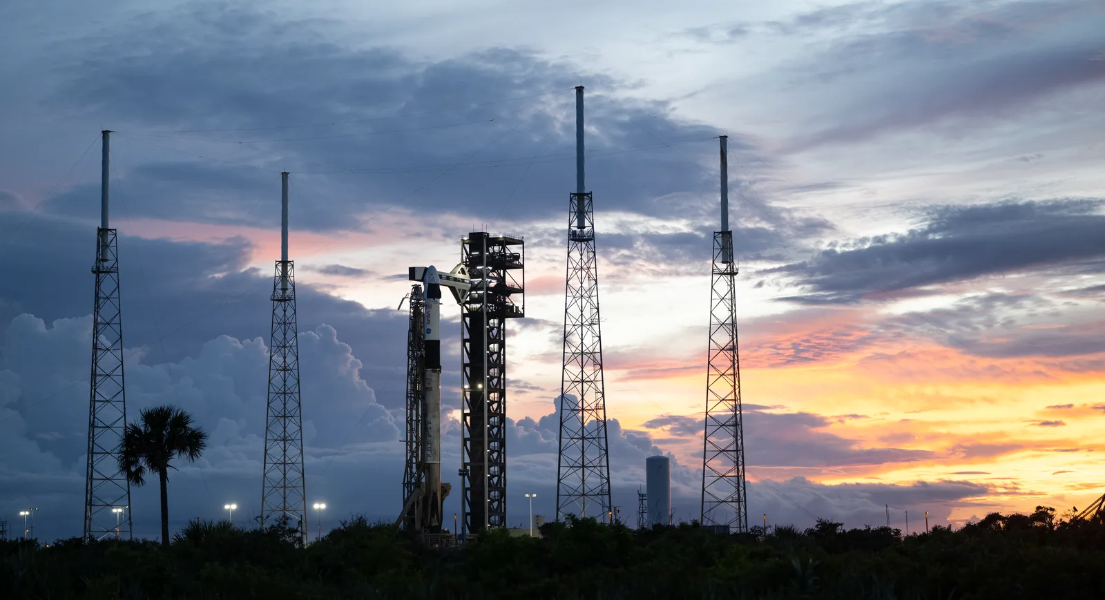 Cohete Falcon 9 con la cápsula Dragon en la plataforma de lanzamiento de Cabo Cañaveral, entre torres de pararrayos, al atardecer
