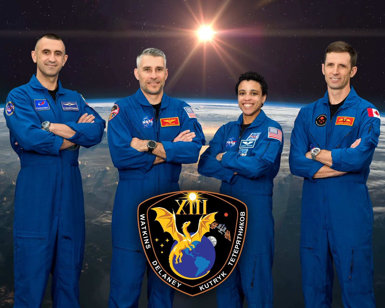 Los cuatro tripulantes de Crew-13, con mono azul y los brazos cruzados, delante de una imagen de la Tierra y con el emblema de la misión