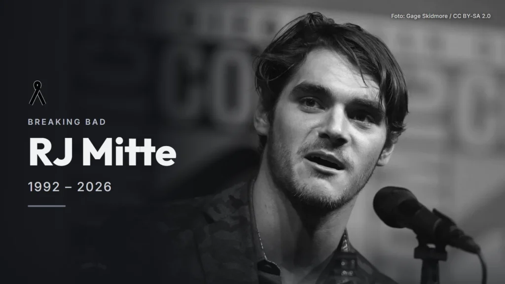 RJ Mitte habla ante un micrófono en el panel del décimo aniversario de Breaking Bad en la Comic-Con de San Diego de 2018, en blanco y negro, junto a su nombre y los años 1992 y 2026