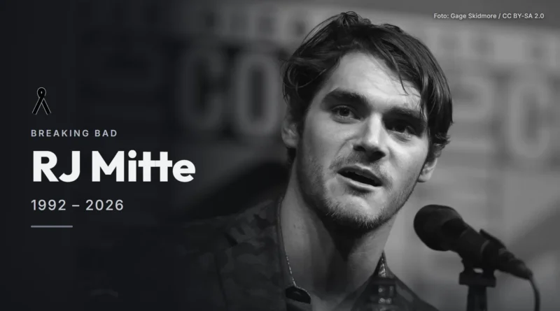 RJ Mitte habla ante un micrófono en el panel del décimo aniversario de Breaking Bad en la Comic-Con de San Diego de 2018, en blanco y negro, junto a su nombre y los años 1992 y 2026