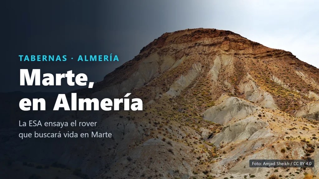 Cerro del desierto de Tabernas con la cima de roca parda en capas y laderas grises surcadas de cárcavas, bajo un cielo nublado, con el texto «Marte, en Almería»